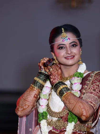 A happy bride adjusting her earring, giving a beautiful glimpse of her intricate and richly stained mehendi.