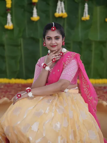 A bride looking lovely at her Haldi ceremony, wearing custom floral jewelry made of red and white flowers that complements her outfit.