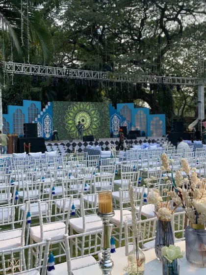 A royal expanse of blue and white for an outdoor sangeet, with rows of white chairs leading to a grand stage inspired by Moroccan and Jaipur aesthetics.