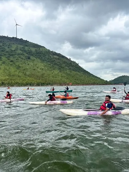 A group of kayakers spreads out across the water at Vani Vilas Sagar, enjoying the freedom and scenery. You can see the windmills on the surrounding hills, a unique feature of this location.