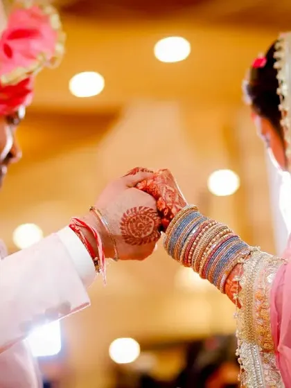 A close-up shot focusing on the couple's hands during a wedding ritual. This detail shot, with their beautiful henna and traditional attire, tells a story of union.