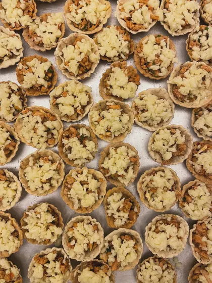 A tray of almond and herb chicken tarts being prepared. The combination of savory chicken, herbs, and crunchy almonds creates a unique texture and flavor.