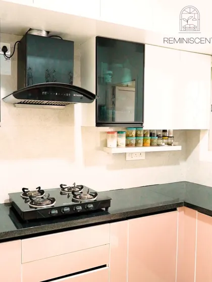 Another angle of the blush pink and white kitchen, showing the placement of the chimney and the open spice rack for easy access. The combination of colors and materials results in a unique and stylish space.
