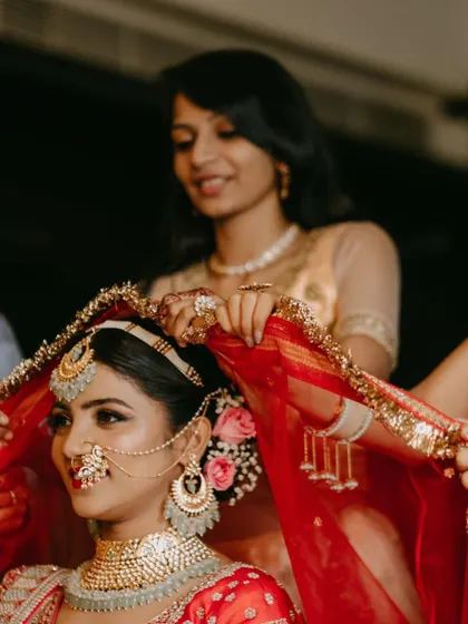 A moment of quiet beauty before the ceremony. The bride is surrounded by her bridesmaids as they help with her red dupatta.