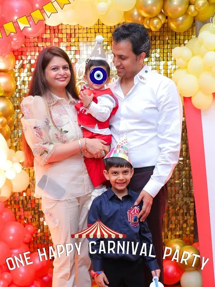 One happy carnival party! The family looks picture-perfect in front of the vibrant shimmer wall and balloon setup at their son's first birthday celebration.