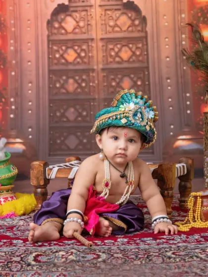 A classic baby Krishna pose, complete with a flute and a curious expression. The detailed setup includes pots, pearls, and a backdrop that looks like a palace doorway.
