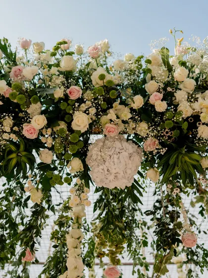 A close-up of a hanging floral installation, rich with white and pink roses, baby's breath, and fresh greenery.