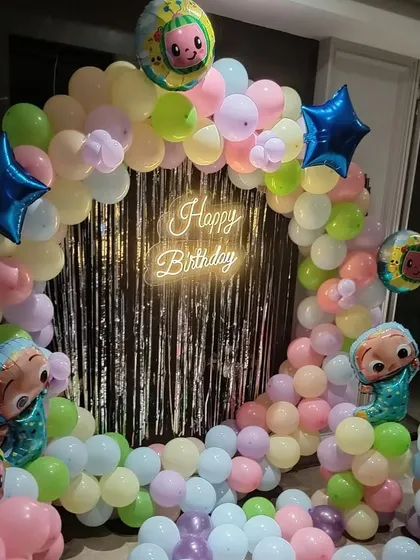A close-up of the Cocomelon balloon arch, highlighting the 'Happy Birthday' neon sign and the star-shaped foil balloons.