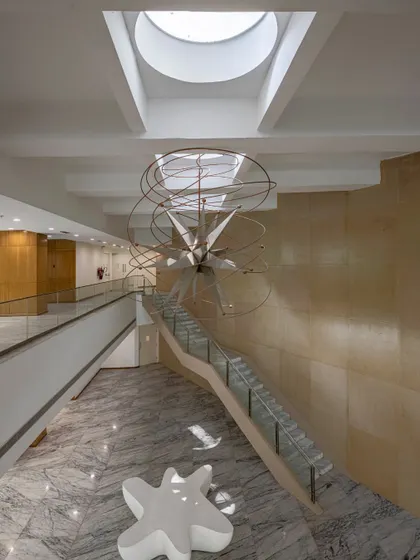 A grand staircase in a double-height lobby, anchored by a sculptural light fixture hanging from a skylight. Here, the staircase acts as a compositional focal point, organizing the space and inviting movement.