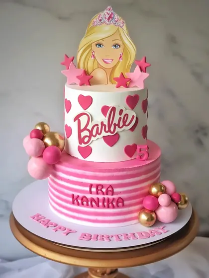 A Barbie-themed whipped cream cake for twins Ira and Kanika. This two-tier cake is all about pink, with hearts, stripes, and a Barbie topper.