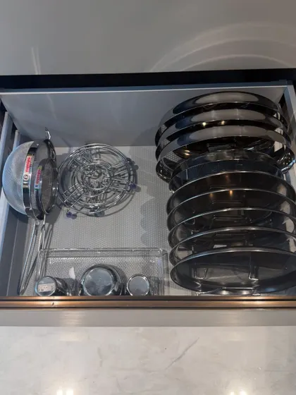 A drawer organized with various steel strainers, lids, and small bowls. We use a vertical rack to file the lids, which is a game-changer for kitchen organization.
