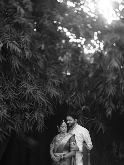 A timeless black and white couple portrait under a canopy of trees. The high-contrast lighting creates a beautiful silhouette effect, emphasizing their connection.