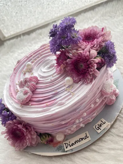A beautiful half-kilo cake with a pink and purple watercolor effect, topped with fresh flowers.