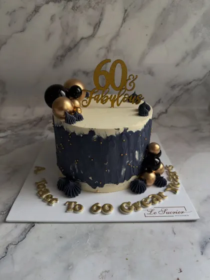 A bold and glamorous cake for a "60 & Fabulous" celebration. The design features a black brushstroke effect against a cream base, decorated with black and gold spheres.