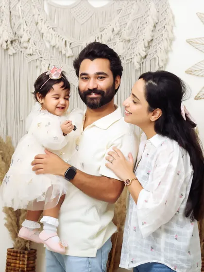 A happy family portrait in the studio. The parents smile lovingly at their cheerful baby girl, capturing a perfect candid moment of family joy.