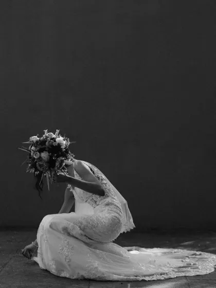 An artistic, high-contrast shot of a bride kneeling, her face hidden by her bouquet. This unconventional portrait is dramatic, emotional, and full of mystery.