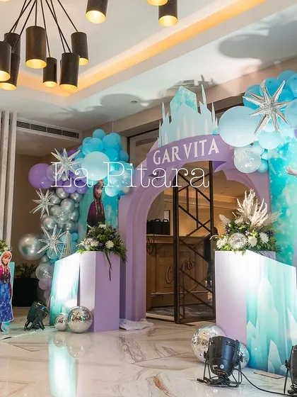 A wide shot of the 'Frozen' party entrance, showing the balloon-adorned archway and welcome sign, setting the stage for the icy adventure inside.
