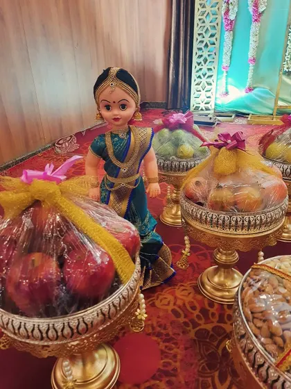 Our traditionally dressed dolls add a charming touch to the platter display. Here, a doll stands beside platters of fresh apples and other fruits, all neatly wrapped for the ceremony.