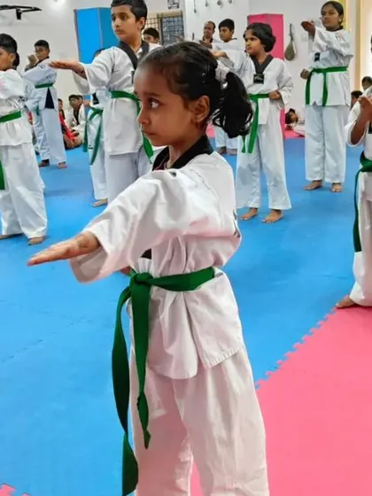 A young girl in the foreground practices a knife-hand block.