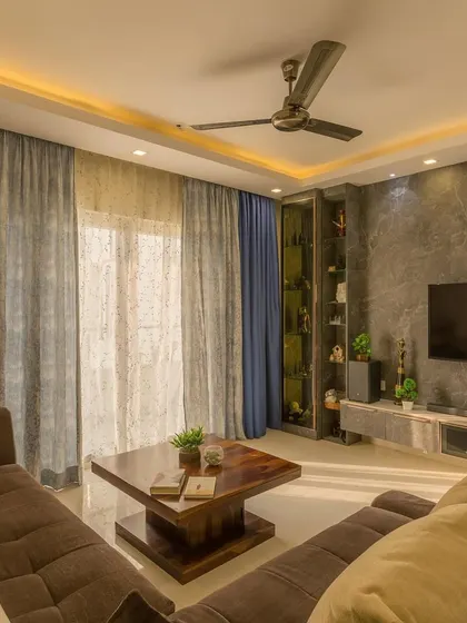 This beautifully designed home features a living room with a plush brown sofa, a dark marble accent wall for the TV, and elegant sheer curtains that let in plenty of natural light.