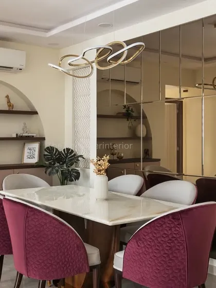 The dining area in the 'Elysian Enclave' project features an arched niche with display ledges and a large tinted mirror wall that visually doubles the space, making it feel grand and open.