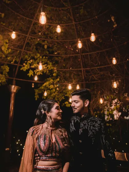 A romantic night portrait of a couple under a canopy of string lights. The warm glow creates an intimate and magical atmosphere for this engagement shoot photo.
