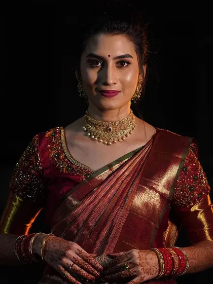 A dramatic and beautiful portrait of a bride in a deep red silk saree. The makeup is focused on glowing skin and a rich lip color, creating a sophisticated look for her reception.