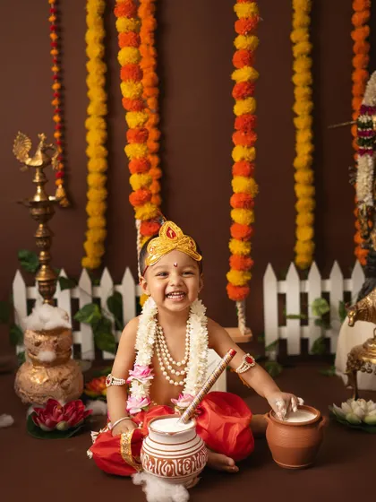 A solo portrait of a laughing little Krishna, enjoying his pot of "butter" in a festive setup.
