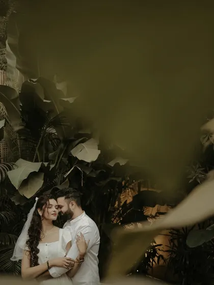 A moody and intimate portrait of a couple surrounded by lush, dark foliage. The creative framing gives the impression of a secret, stolen moment in a hidden paradise.