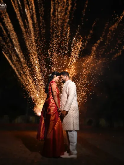 A couple shares an intimate moment, their faces illuminated by a brilliant explosion of fireworks behind them. This night shot from a wedding celebration captures the magic and energy of the festivities with dramatic lighting.