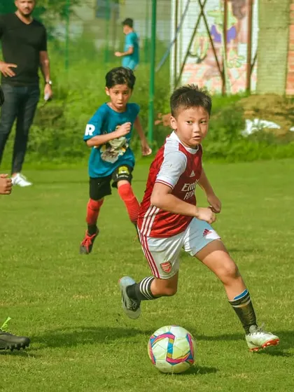 A young player in an Arsenal-style kit dribbles with speed.