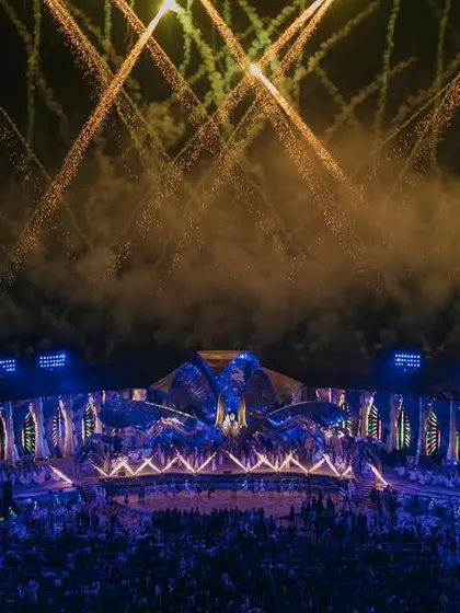A moment of magic under a sky of sparks. This wide shot captures the epic scale of a concert-style wedding event, complete with a massive stage and a stunning fireworks display.