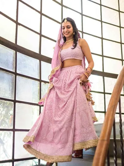 The bride descending the stairs in her home, looking joyful and radiant in her pink lehenga.