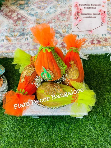 Coconuts wrapped in vibrant orange and green net fabric with gold embroidery. This is a colorful and festive way to present coconuts for any pooja or ceremony.