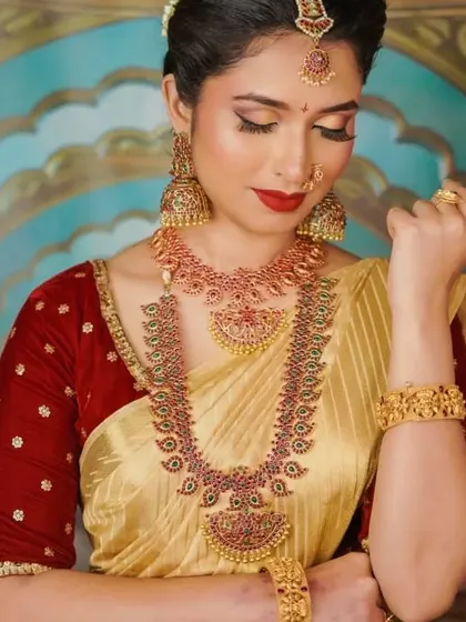 This is a beautiful example of a complete traditional look, perfect for a wedding guest or for a special puja. The makeup features a classic red lip and defined eyes, paired with stunning temple jewellery.