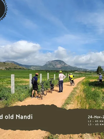 The 'Good old Nandi' tour is a classic for a reason. This image shows riders on a trail through green fields with the iconic Nandi Hills in the background.