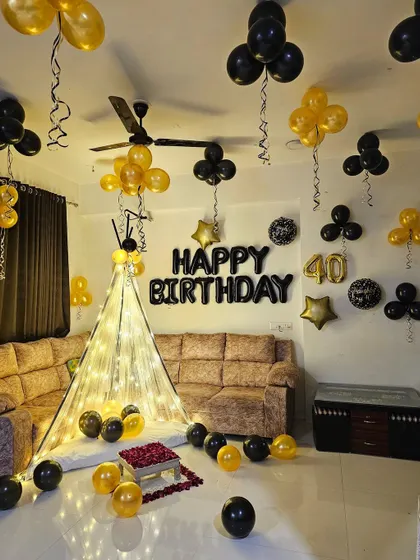 A cozy 40th birthday celebration at home, featuring a small cabana, gold and black balloons, and '40' foil balloons on the wall.