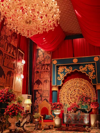 A regal seating area featuring a throne-like chair, intricate wall panels with traditional Indian art, and a massive carved medallion. This vignette is a perfect example of creating immersive, story-rich corners within a larger event.