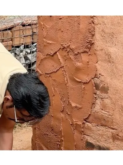 A close-up still of an artisan applying the Thappi plaster, showcasing the rich, earthy color and rough texture of the initial coat.