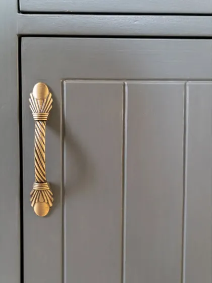 A close-up of the ornate brass handle on the desk's cabinet, adding a touch of vintage elegance to the piece.