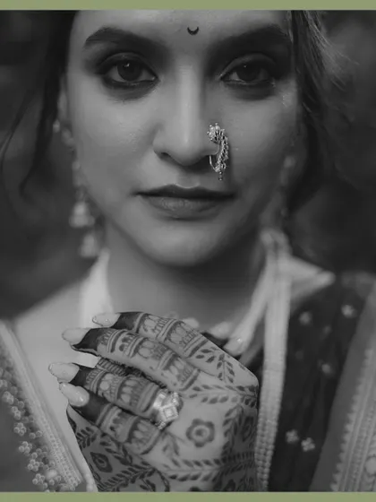 A powerful black and white portrait of a Maharashtrian bride. The focus is on her expressive eyes, traditional nath, and the intricate mehndi on her hands, creating a timeless and soulful image.