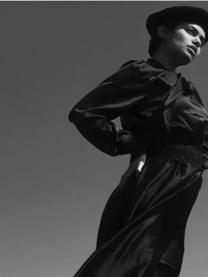 A high-fashion outdoor shoot in black and white. The makeup is clean and sculpted to stand out against the bright sky, creating a strong, graphic silhouette.