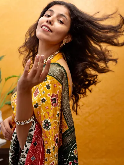 A dynamic, candid shot with hair in motion, bringing energy and life to this traditional yellow Patola saree.