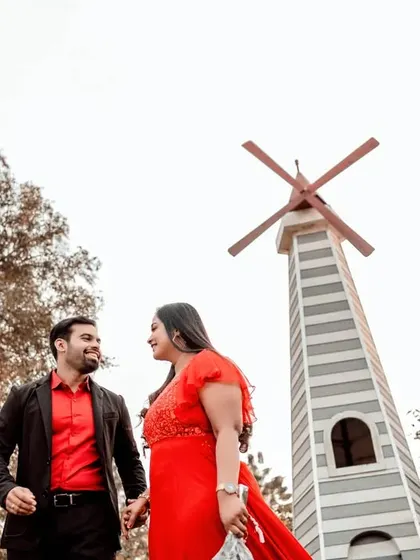 A low-angle shot of a couple with a windmill in the background, creating a grand and romantic feel for their pre-wedding portrait.