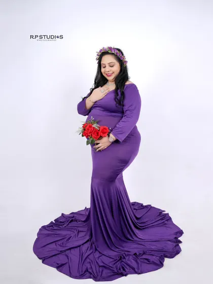 A classic pose with a pop of color. The mom-to-be holds a bouquet of red roses that contrasts beautifully with her elegant purple gown and floral crown.