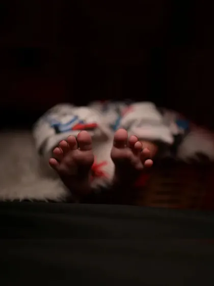 A detailed shot focusing on the newborn's tiny toes. The dark, moody lighting creates an artistic and intimate feel, emphasizing the delicate features of the baby.