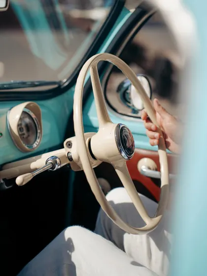 A glimpse into the driver's seat of a vintage Fiat, focusing on the hands on the classic steering wheel. It's a personal, human touch in a series about machines.