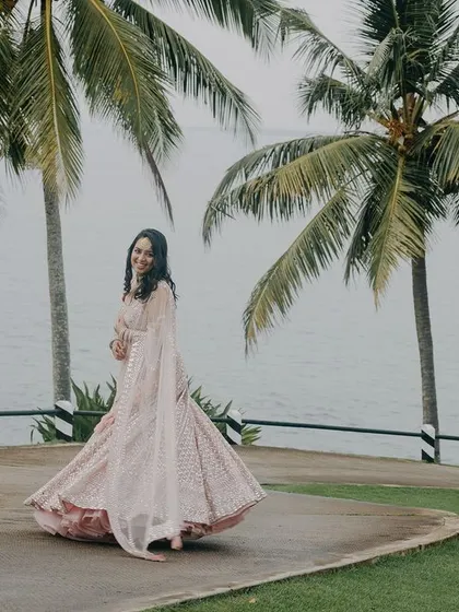 A joyful bridal portrait in a stunning destination. The bride's twirl shows off her beautiful pink lehenga against the backdrop of palm trees and the sea in Kerala, capturing a moment of pure happiness.