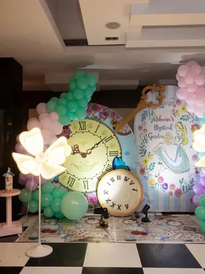A whimsical photo booth for an 'Alice in Wonderland' theme, featuring giant clocks, a custom backdrop, and glowing flower props for a magical touch.