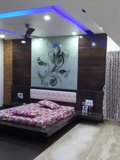 A dramatic bedroom design featuring a floating bed and a large, back-painted glass panel with a floral etching behind the headboard. The false ceiling incorporates blue cove lighting, adding a cool, ambient glow to the room.